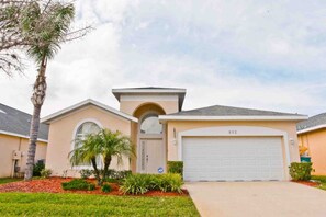 A single-story house with a garage, a front yard with landscaping, and a clear sky. - Crystal Cove 932 (Kissimmee)