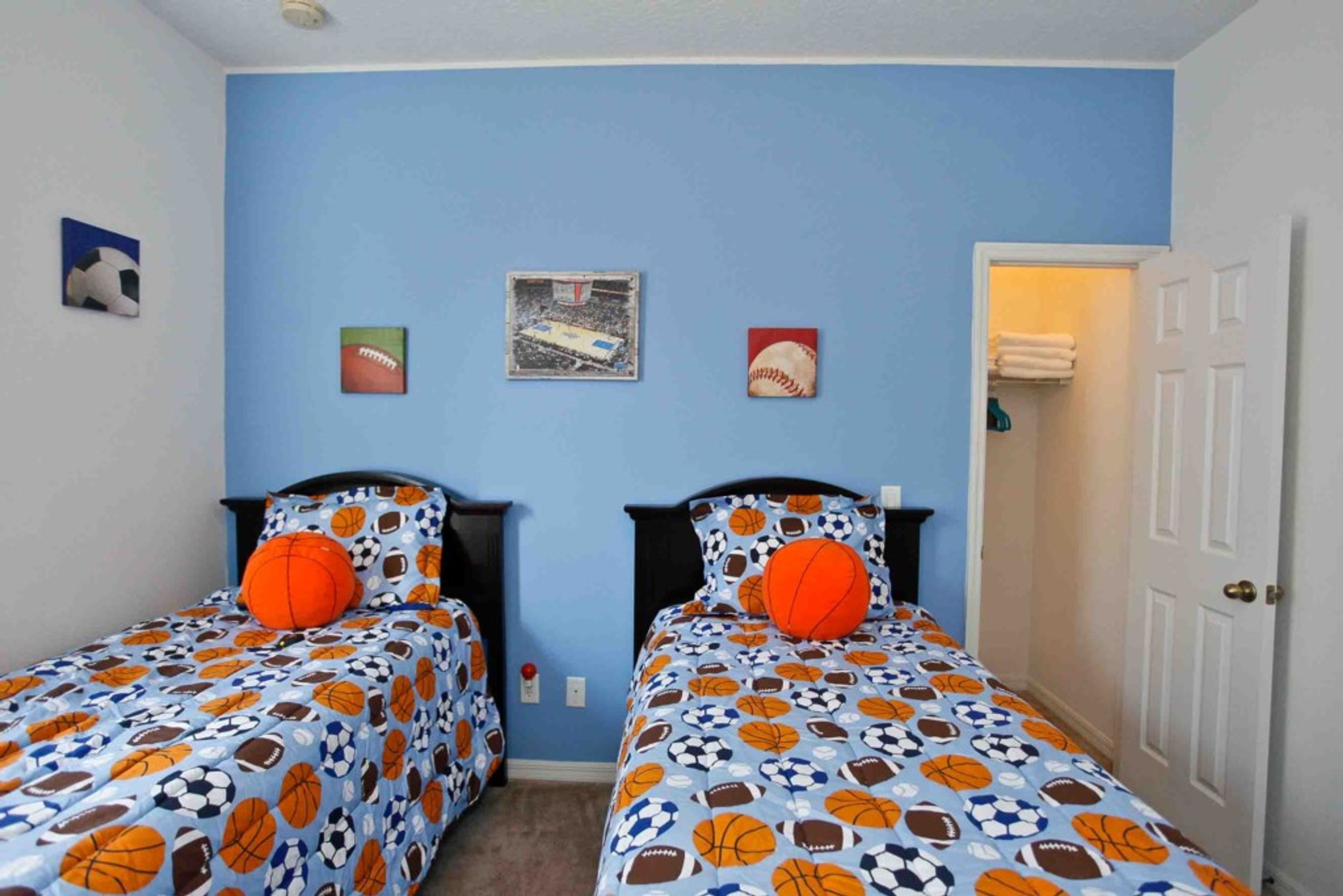 Habitación con dos camas, cada una con pared azul y edredón estampado. Se observan cuadros en la pared y una puerta a la derecha.