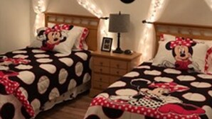 Een slaapkamer met twee bedden, elk met een dekbedovertrek met Mickey Mouse en Minnie Mouse thema, een nachtkastje met een lamp, en een muur met Minnie Mouse decoraties.