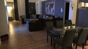 Een moderne woonkamer met een donkere bank, een glazen salontafel en een eethoek met een donkere tafel en stoelen.