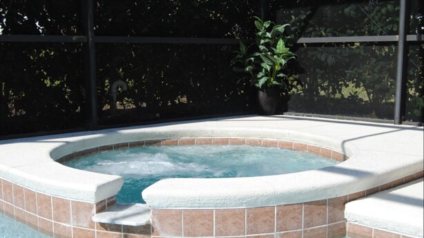 Een jacuzzi met betegelde rand en treden die naar het water leiden, omringd door een hek en een bloempot.