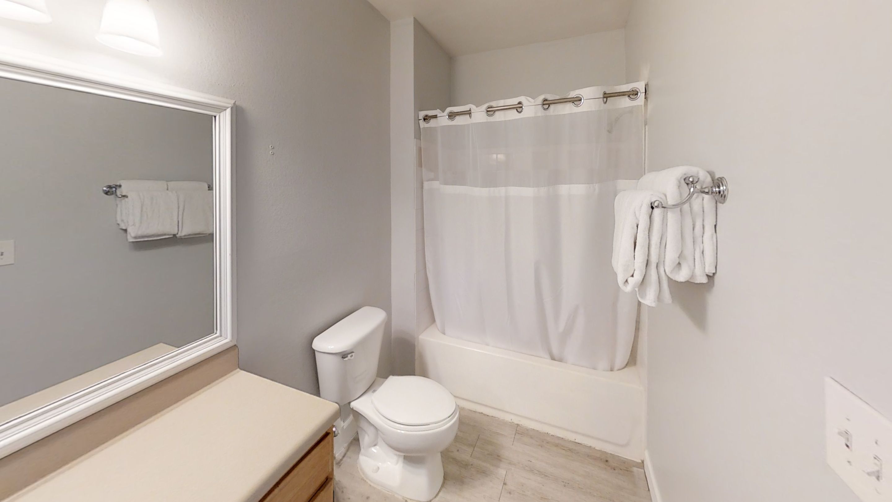 A bathroom with a toilet, a bathtub with a shower curtain, and a mirror above the sink.