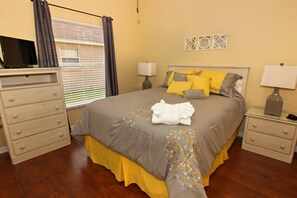 Una camera da letto con un letto, comodini, una cassettiera, una televisione e una finestra con tende.