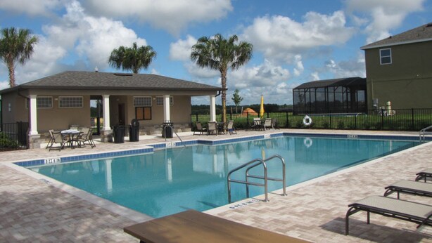 A swimming pool with a tiled deck, lounge chairs, and a covered seating area. - Laurel Estates 133 (Davenport)