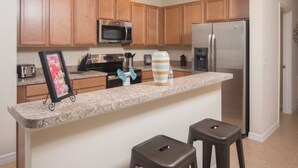 A kitchen with wooden cabinets, a stainless steel refrigerator, a microwave, and a granite countertop. - Laurel Estates 133 (Davenport)