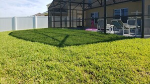 A modern building with a glass enclosure, a well-maintained lawn, and outdoor seating with a flamingo decoration. - Laurel Estates 133 (Davenport)