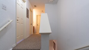A narrow hallway with carpeted stairs, white walls, and a door at the end. - Villas at Seven Dwarfs 4601 B8.106 (Kissimmee)