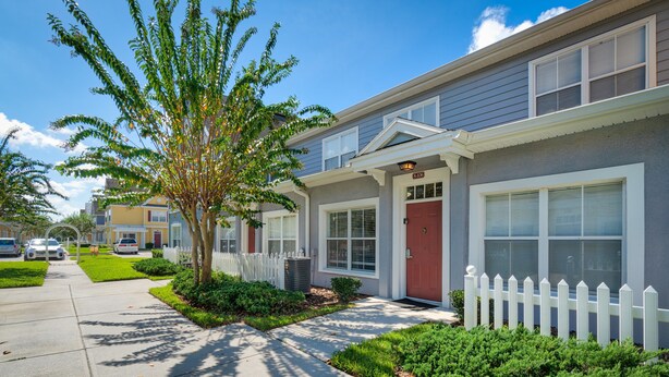 A residential building with a red door, white picket fence, and a well-maintained lawn. - Villas at Seven Dwarfs 4601 B8.106 (Kissimmee)