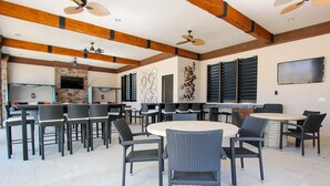 A spacious outdoor dining area with multiple tables and chairs, ceiling fans, and a stone fireplace. - Solterra 5180 B (Davenport)