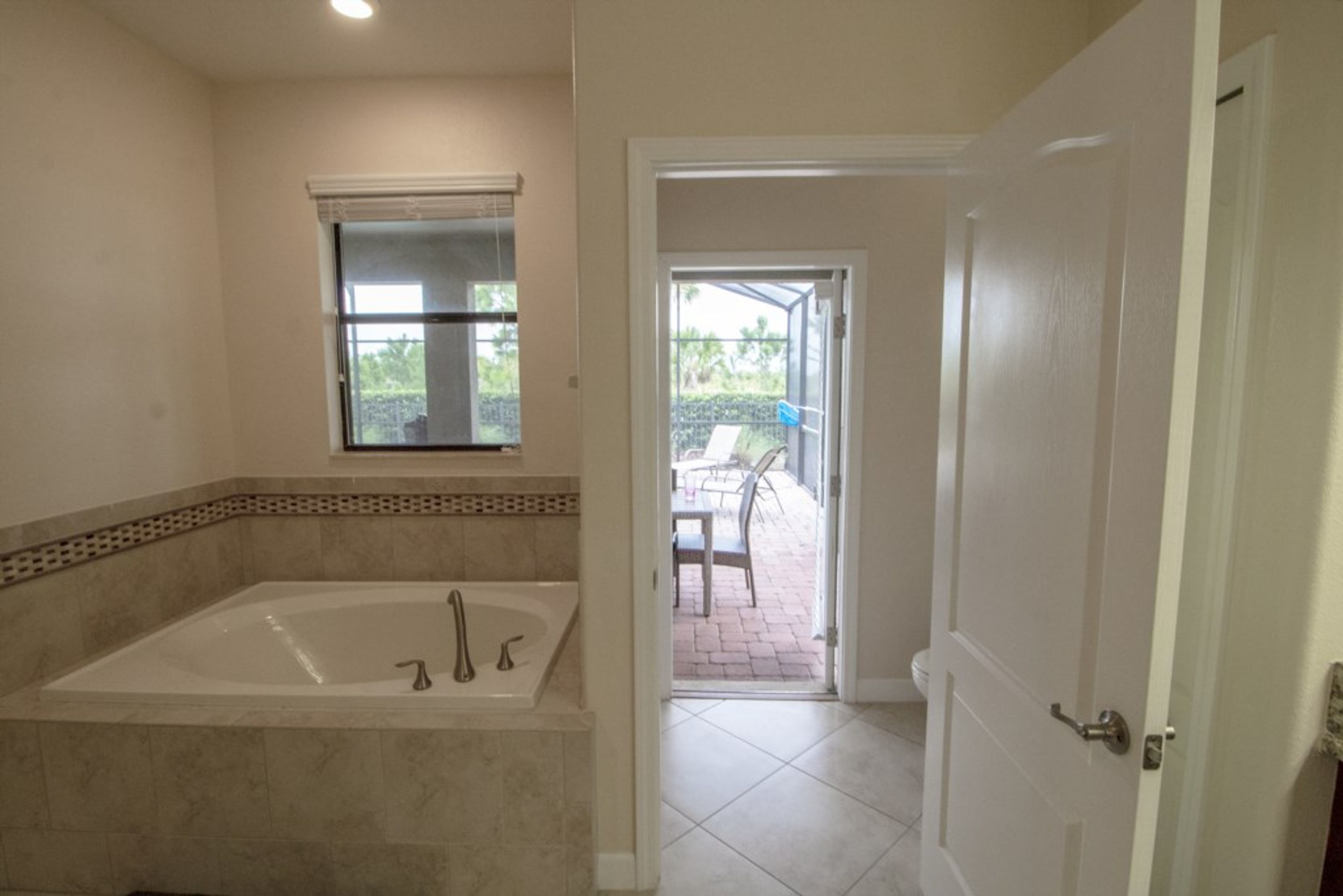 A bathroom with a large bathtub, a window, and a door leading to an outdoor patio area.