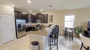 A modern kitchen with dark cabinets, stainless steel appliances, a granite countertop, and a dining area with a table and chairs. - Solterra 5180 B (Davenport)