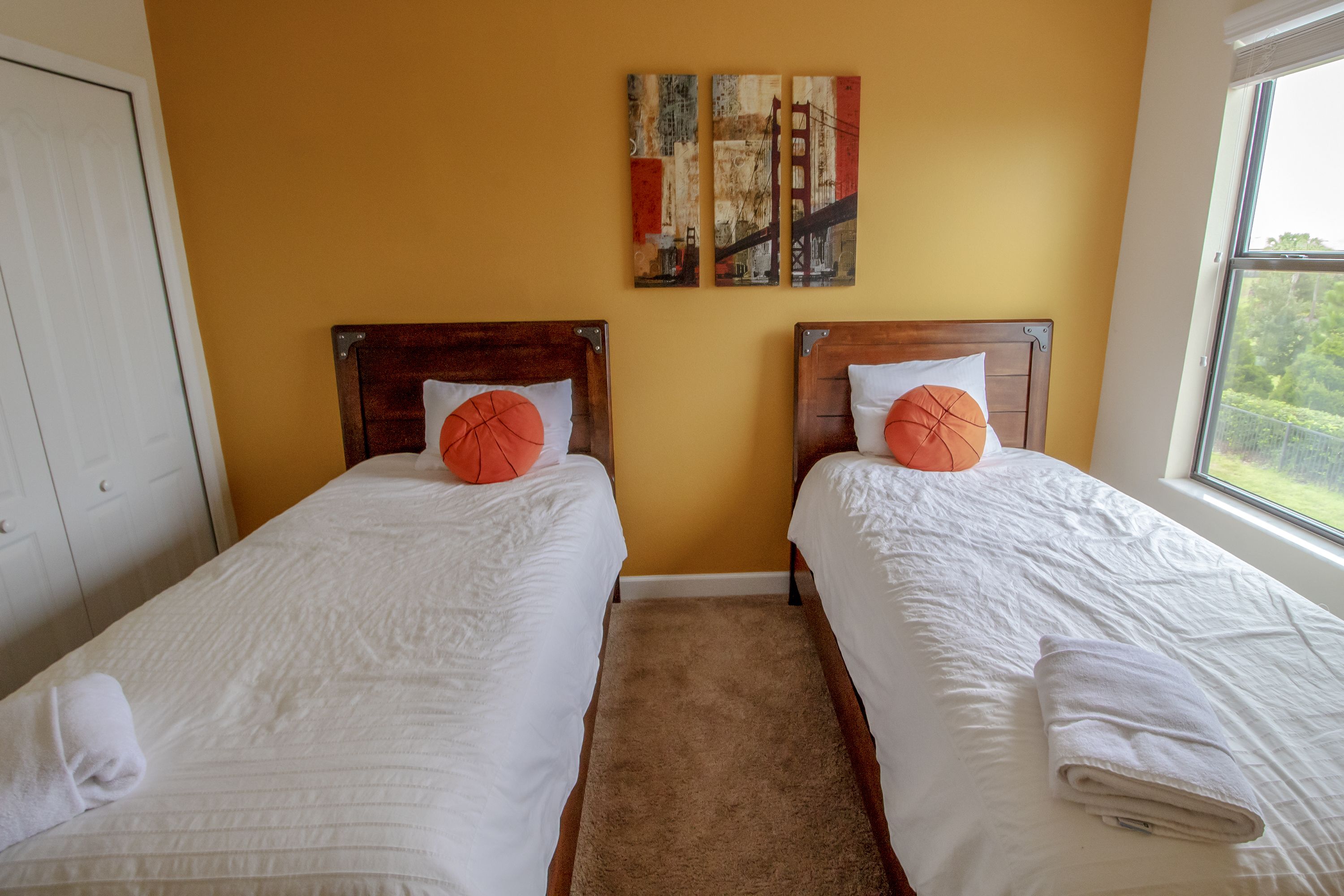 A hotel room with two single beds, a brown carpet, and a window with a view of greenery.