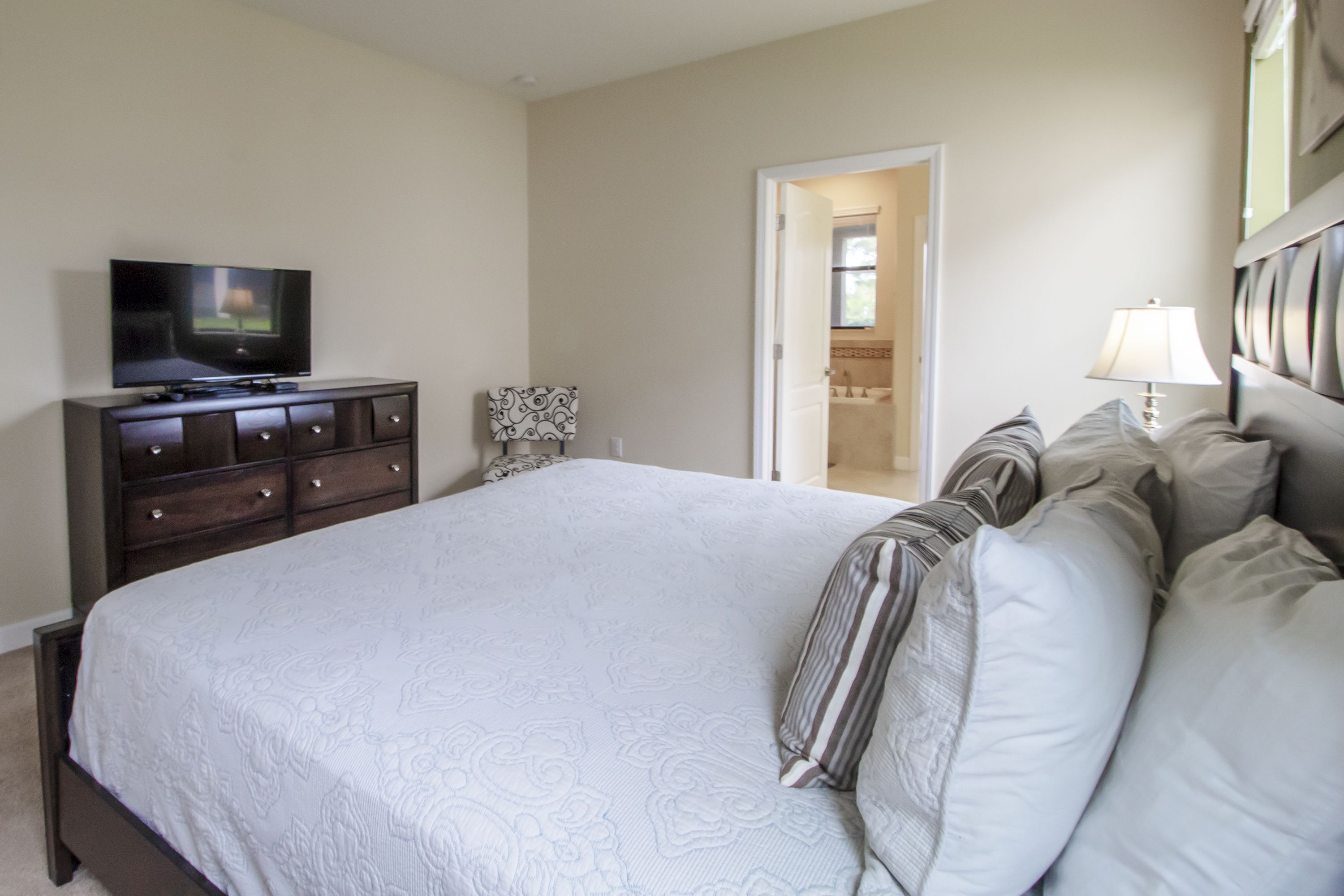 Un dormitorio con una cama grande, un aparador, un televisor y una puerta que da a un baño.