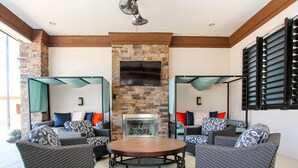 A cozy outdoor seating area with wicker furniture, a stone fireplace, and a TV mounted on the wall. - Solterra 5180 B (Davenport)