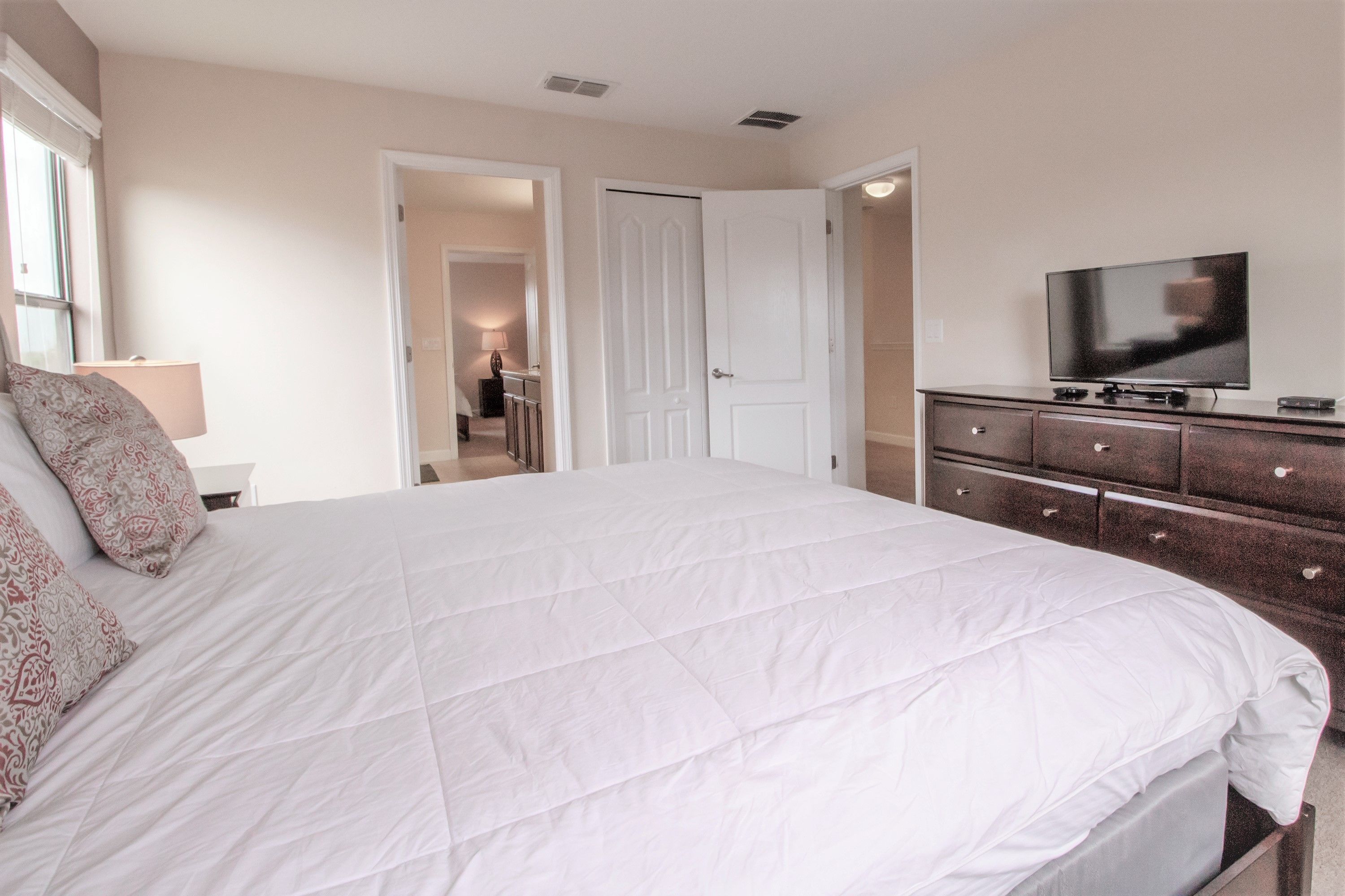 Une chambre à coucher avec un grand lit, une commode, un téléviseur et une porte donnant sur une autre pièce.