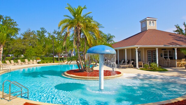 A swimming pool with a water fountain, palm trees, and a building with a red roof. - Lucaya Village 2905 - 101 (Kissimmee)