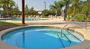 A swimming pool with a tiled edge, surrounded by lounge chairs and palm trees.