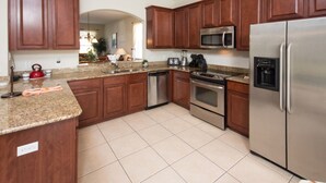 A modern kitchen with wooden cabinets, stainless steel appliances, granite countertops, and a tiled floor. - Windsor Hills 2583 (Kissimmee)