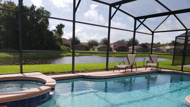 A swimming pool with a hot tub, surrounded by a covered area with chairs, and a view of a residential neighborhood. - Sandy Ridge 922 (Davenport)