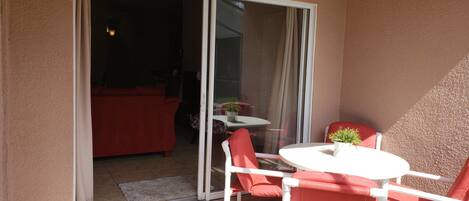 A balcony with a ceiling fan, a sliding glass door, a red sofa, and a small table with chairs.