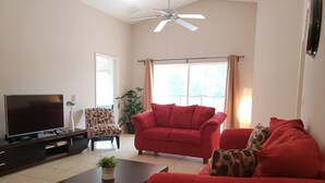 A living room with a flat-screen TV, a red sofa, a patterned armchair, and a coffee table. - Sandy Ridge 922 (Davenport)