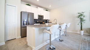 A modern kitchen with white cabinets, stainless steel appliances, and a central island with bar stools. - Storey Lake 4953 (Kissimmee)