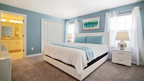 A bedroom with a bed, nightstands, a lamp, a painting, and a door leading to a bathroom. - Storey Lake 4953 (Kissimmee)