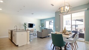 A modern kitchen with a central island, a dining area with a table and chairs, a living room with a sofa, and a large window providing natural light. - Storey Lake 4953 (Kissimmee)