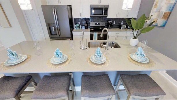 A modern kitchen with a central island, stainless steel appliances, and bar stools. - Champions Gate 8988 (Davenport)