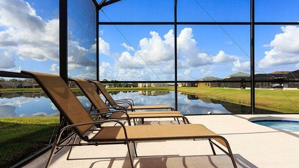 Zona junto a la piscina con sillones de descanso y vistas a un lago y edificios a lo lejos.