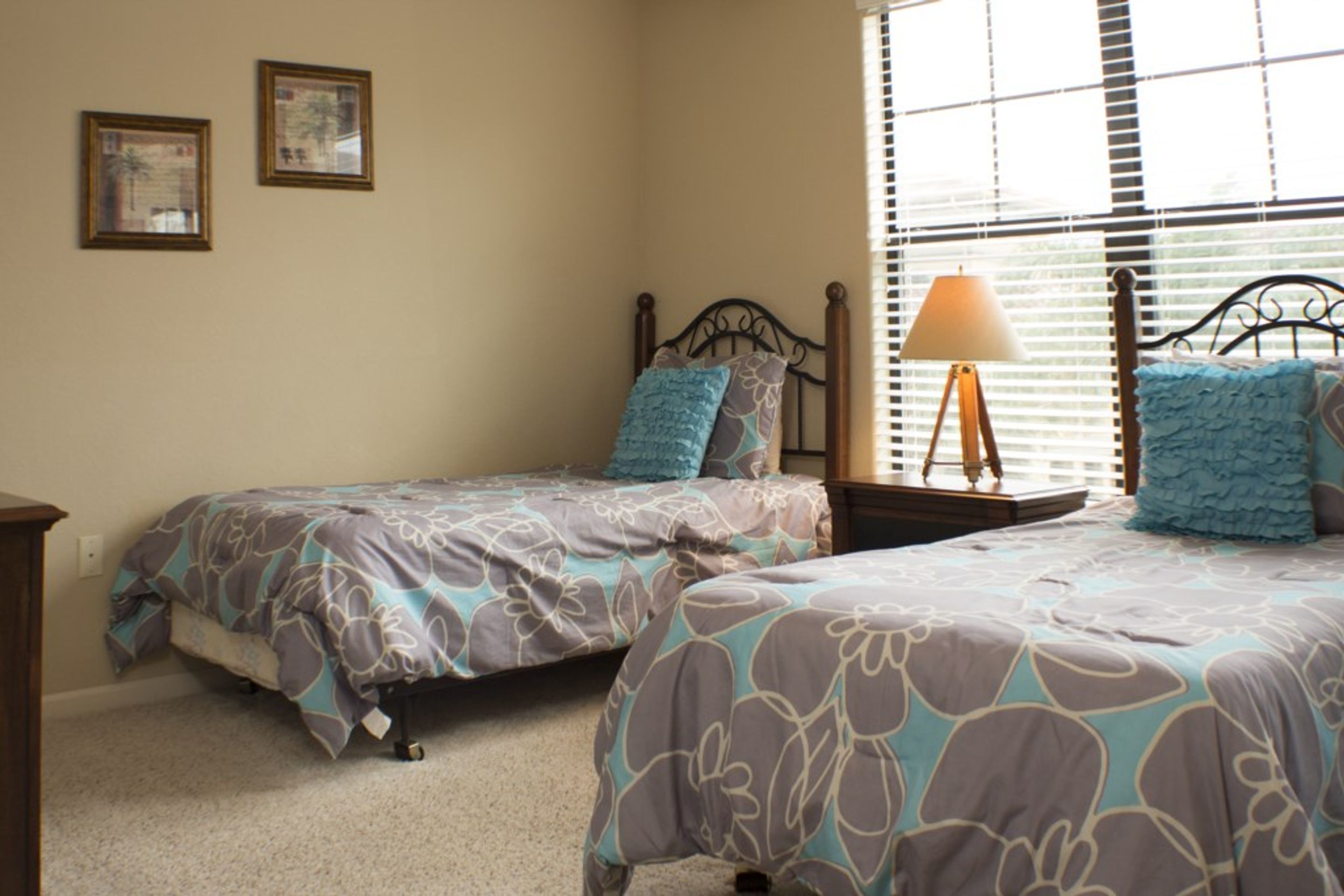 A bedroom with two single beds, a nightstand with a lamp, and a window with blinds.