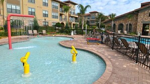 A swimming pool with two yellow water slides, surrounded by a brick walkway and a black fence. - Bella Piazza 904 - 527 (Davenport)
