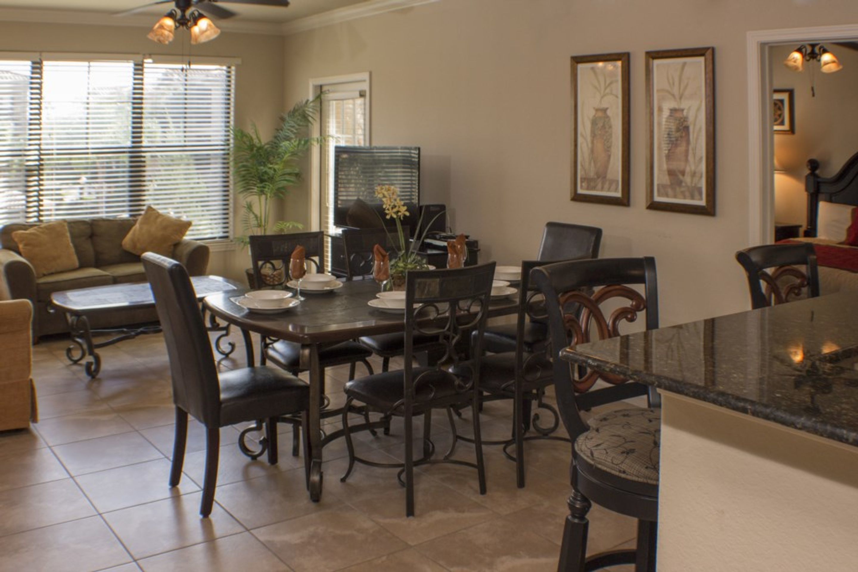 A dining area with a wooden table and chairs, a sofa, and a plant.