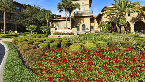 A hotel with a landscaped garden, a sign reading "Bella Piazza," and a stone building with a balcony. - Bella Piazza 904 - 527 (Davenport)
