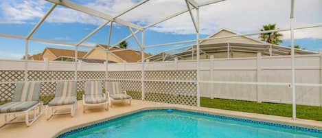 A covered outdoor swimming pool with lounge chairs and a white fence.
