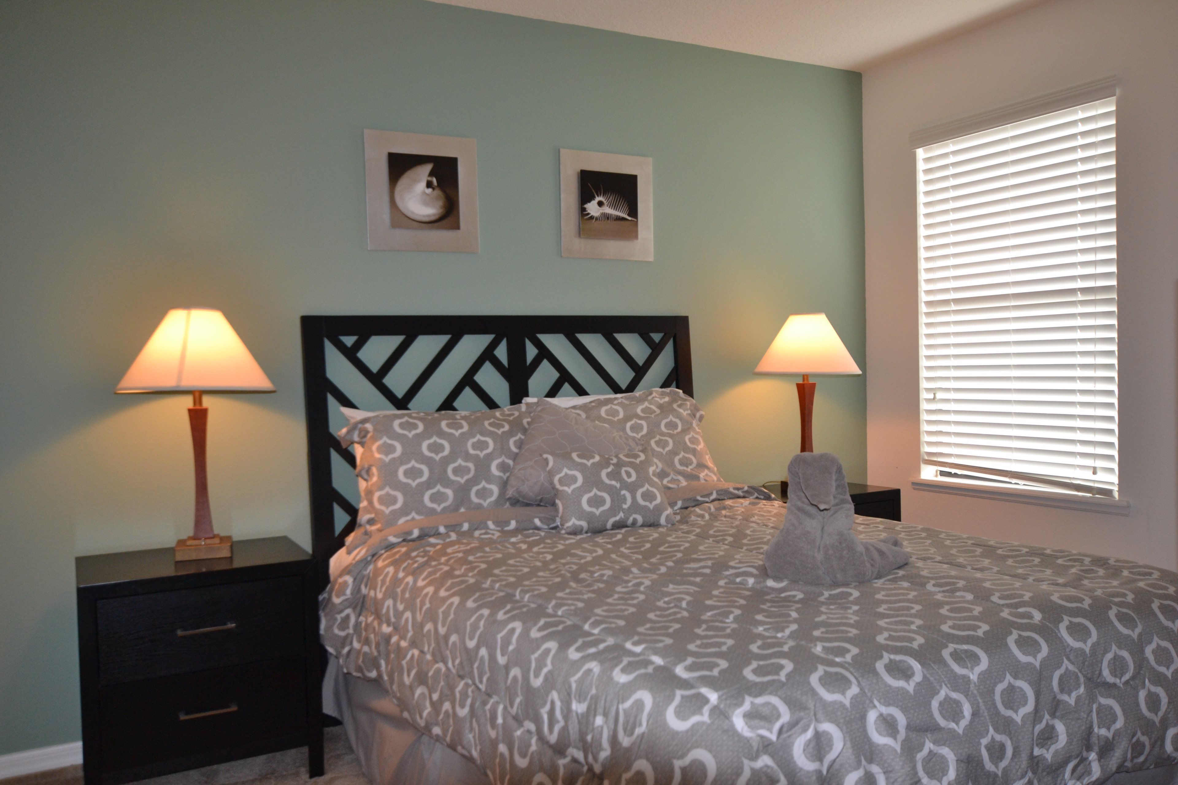 A bedroom with a bed, two nightstands, two lamps, and two wall art pieces.