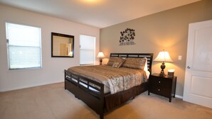 A bedroom with a bed, two bedside tables with lamps, a door, and a wall with a floral decoration. - Cypress Pointe 1151 (Davenport)