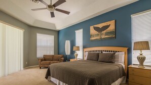 A bedroom with a large bed, a ceiling fan, a wooden headboard, a brown armchair, bedside lamps, and a wall painting. - Highlands Reserve Golf & Country Club 520 (Davenport)