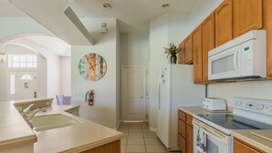 A modern kitchen with wooden cabinets, a white refrigerator, a microwave, an oven, and a sink. - Highlands Reserve Golf & Country Club 520 (Davenport)