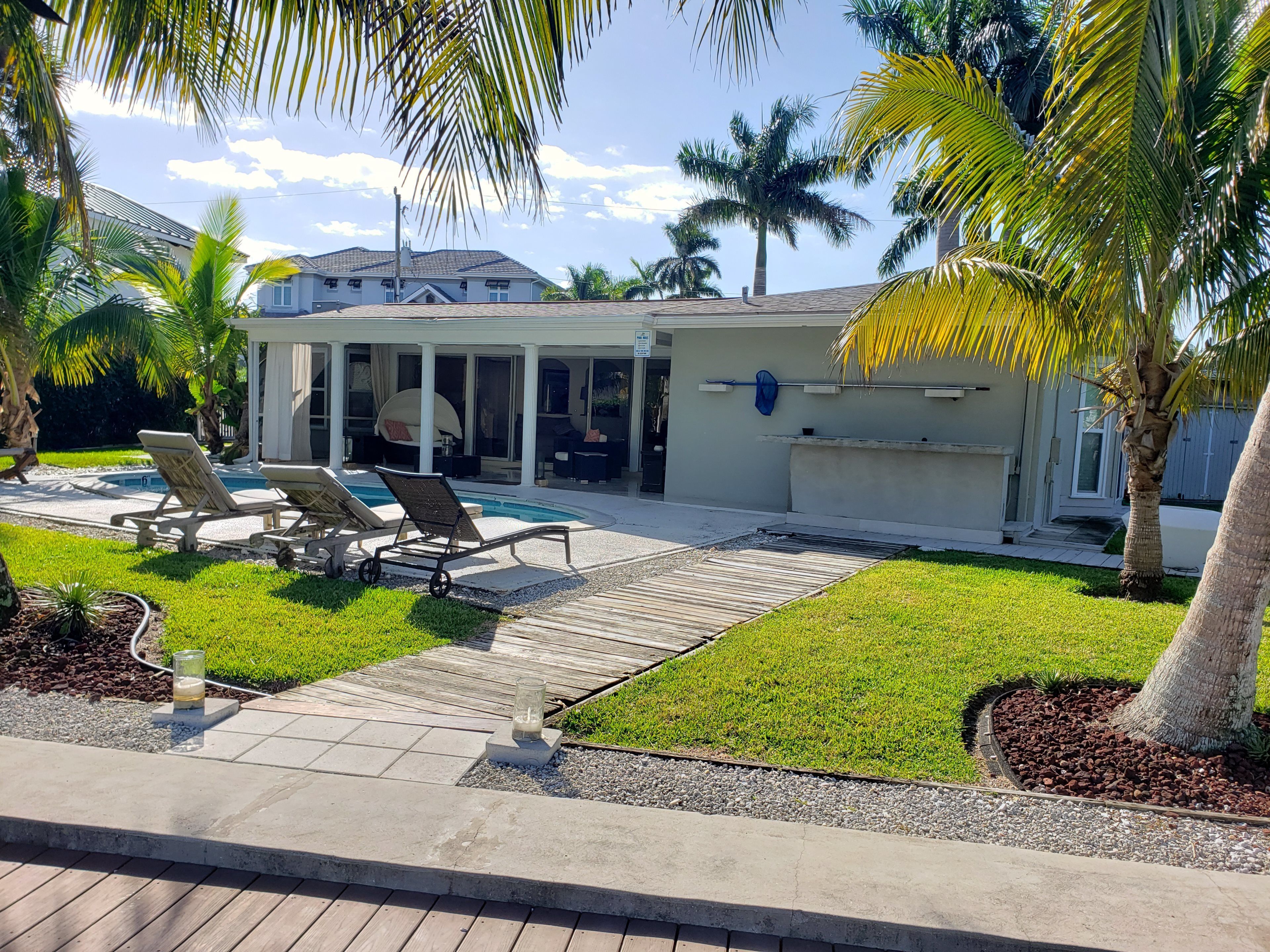 A poolside area with lounge chairs, a covered patio, and a house in the background.