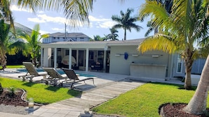Un espace aménagé au bord de la piscine, avec des chaises longues, un patio couvert et une maison en arrière-plan.