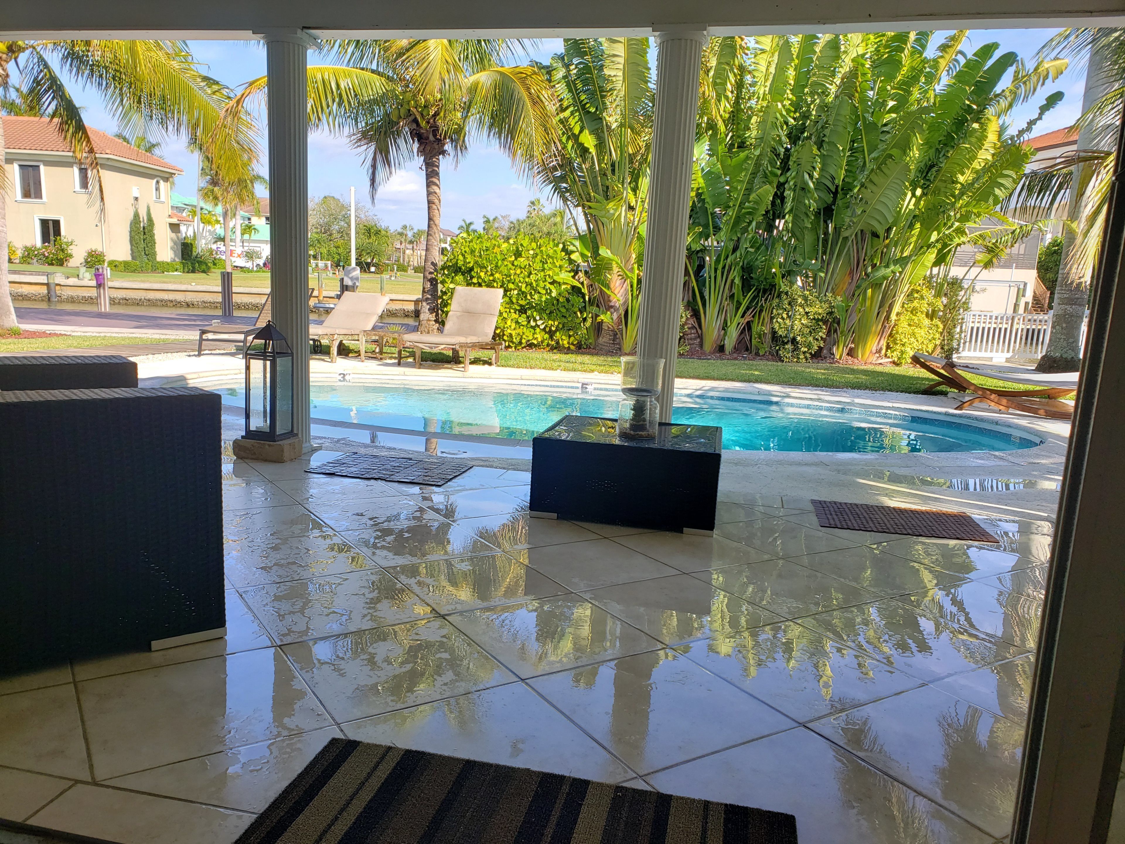 A poolside area with a tiled floor, lounge chairs, and a view of a swimming pool.