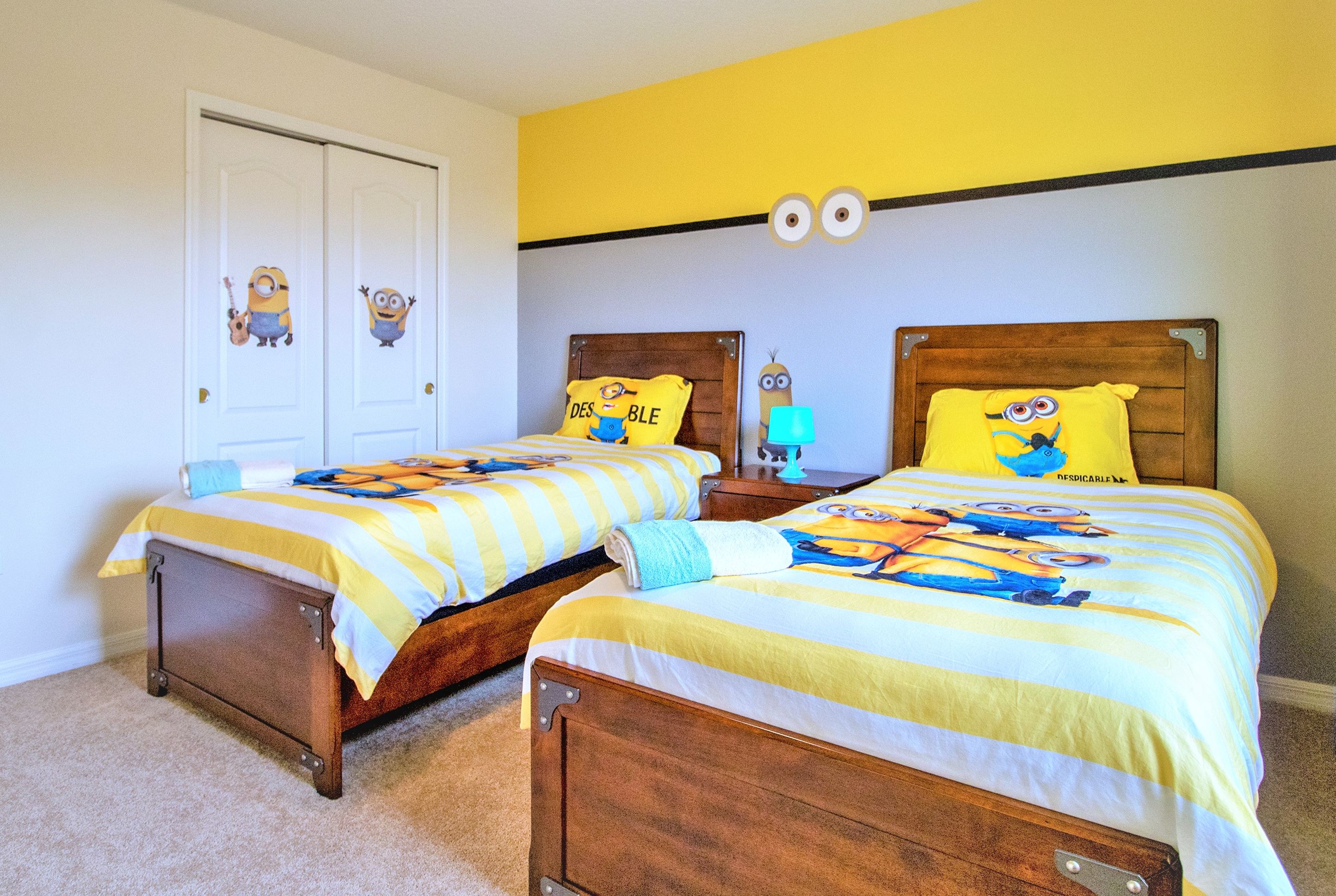 A bedroom with two wooden beds, each with a yellow and white striped bedspread featuring Minion characters.
