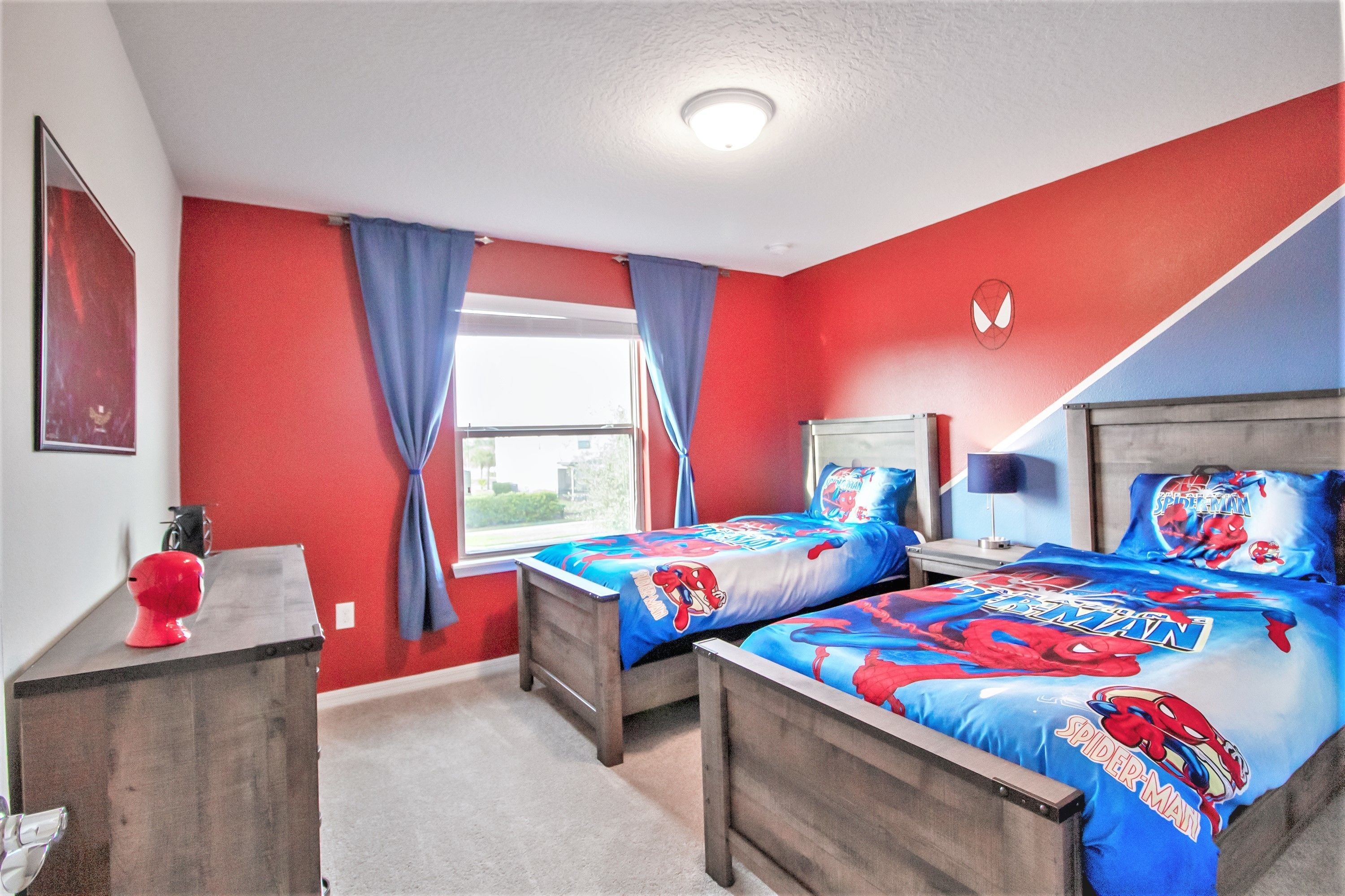 A bedroom with two beds, red walls, and a window with blue curtains.