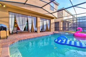 An outdoor swimming pool with a pink flamingo float and a blue step ladder. - Windsor at Westside 1852 (Kissimmee)