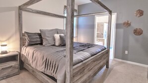Ein Himmelbett mit Holzrahmen, grauer Bettwäsche und einem Nachttisch mit Lampe.