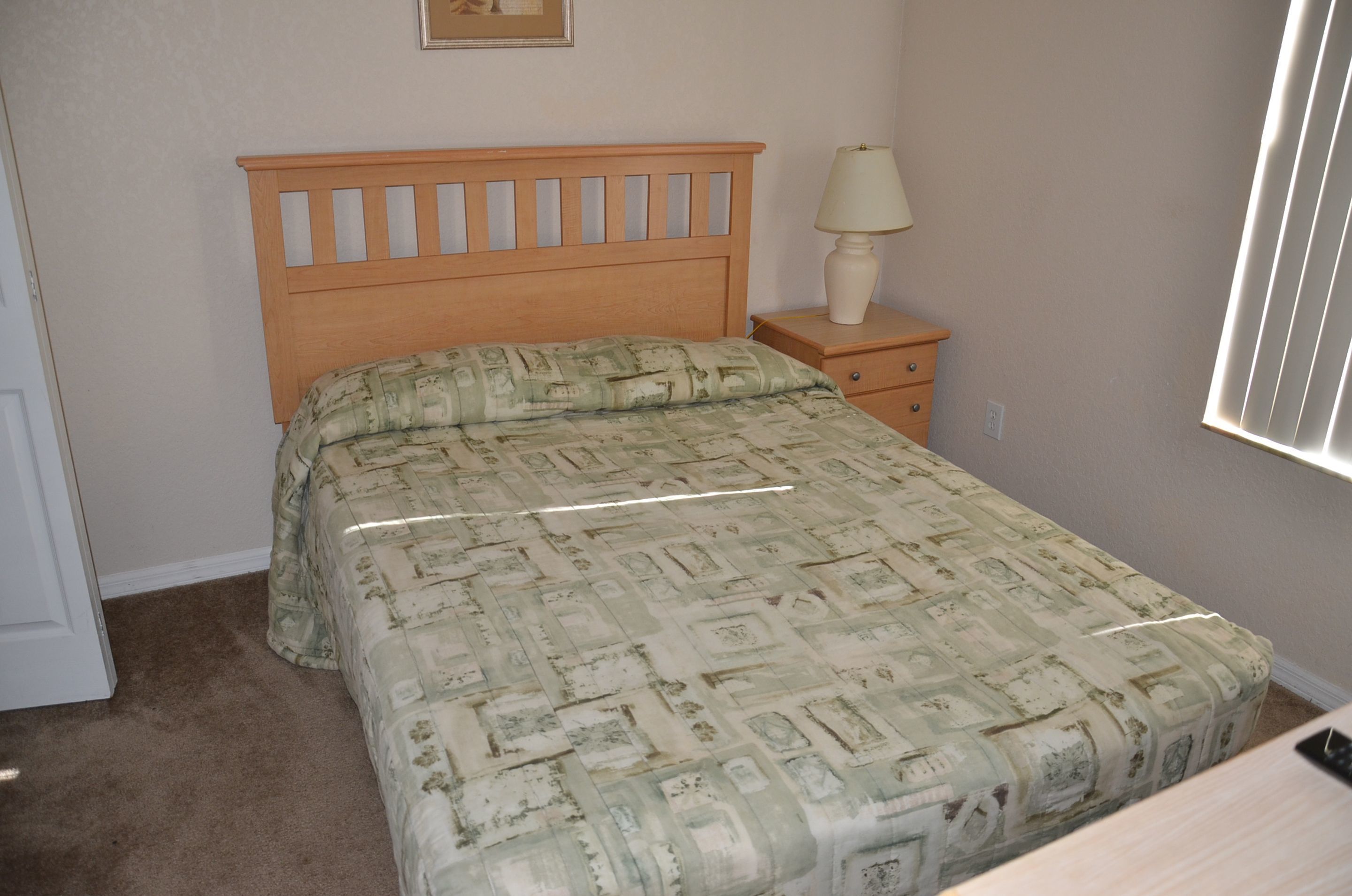 A bedroom with a wooden headboard, a bedside table with a lamp, and a patterned bedspread.