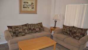 Ein Wohnzimmer mit zwei beigefarbenen Sofas, einem Holztisch, einer Lampe und einem gerahmten Bild an der Wand.