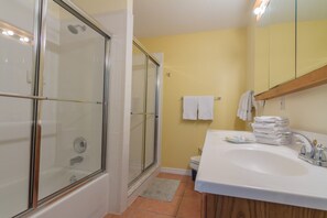 A bathroom with a glass-enclosed shower, a white sink, and a yellow wall.