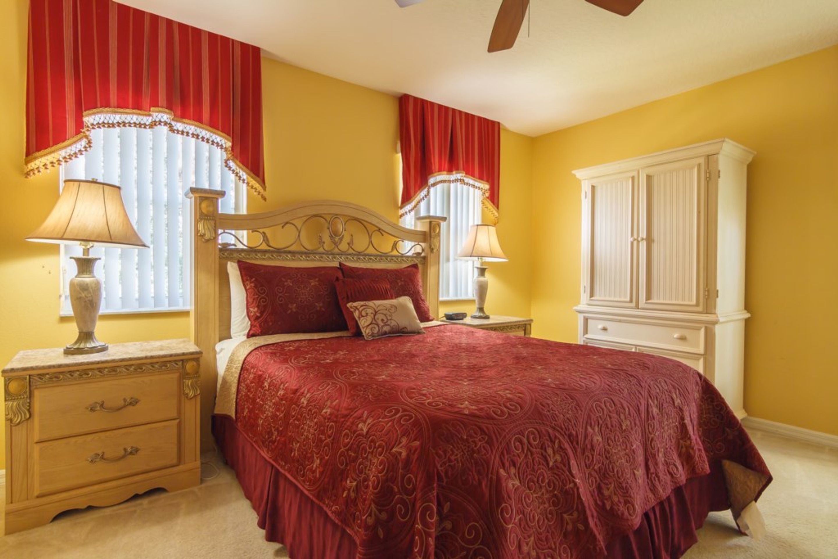 A bedroom with a large bed, two bedside tables with lamps, a nightstand with drawers, and a white wardrobe.